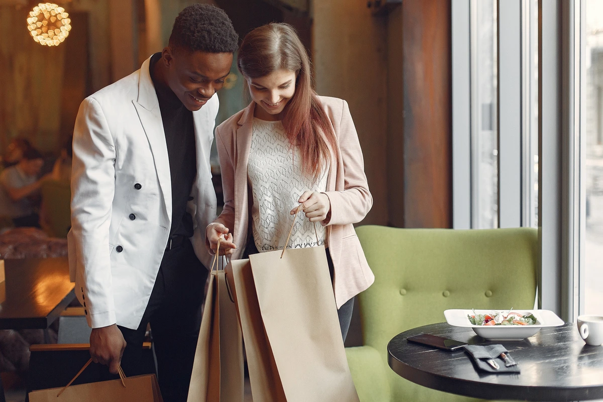 Casal elegante sorrindo e olhando sacolas de compras em restaurante moderno.