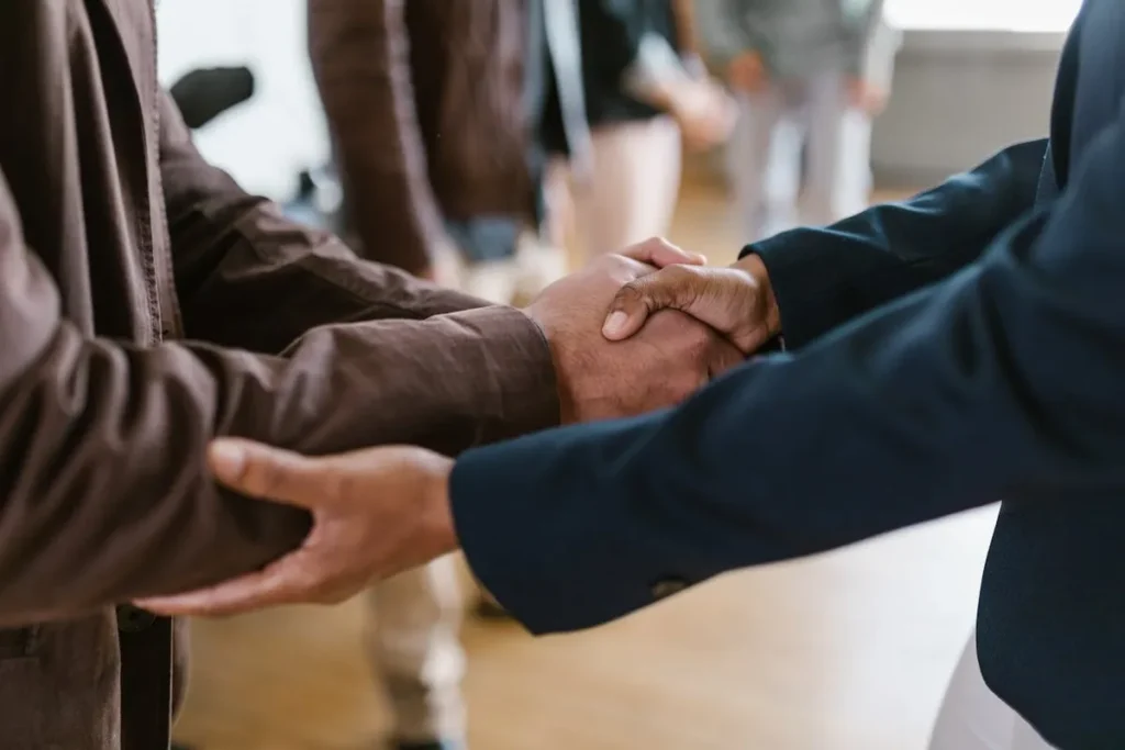 Apertos de mão entre duas pessoas, uma vestindo um casaco marrom e a outra um blazer azul-marinho, simbolizando uma conexão e o sucesso do marketing de relacionamento.