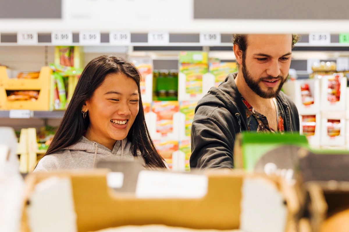 Casal sorridente fazendo compras em mercados atacadistas, escolhendo produtos nas prateleiras.