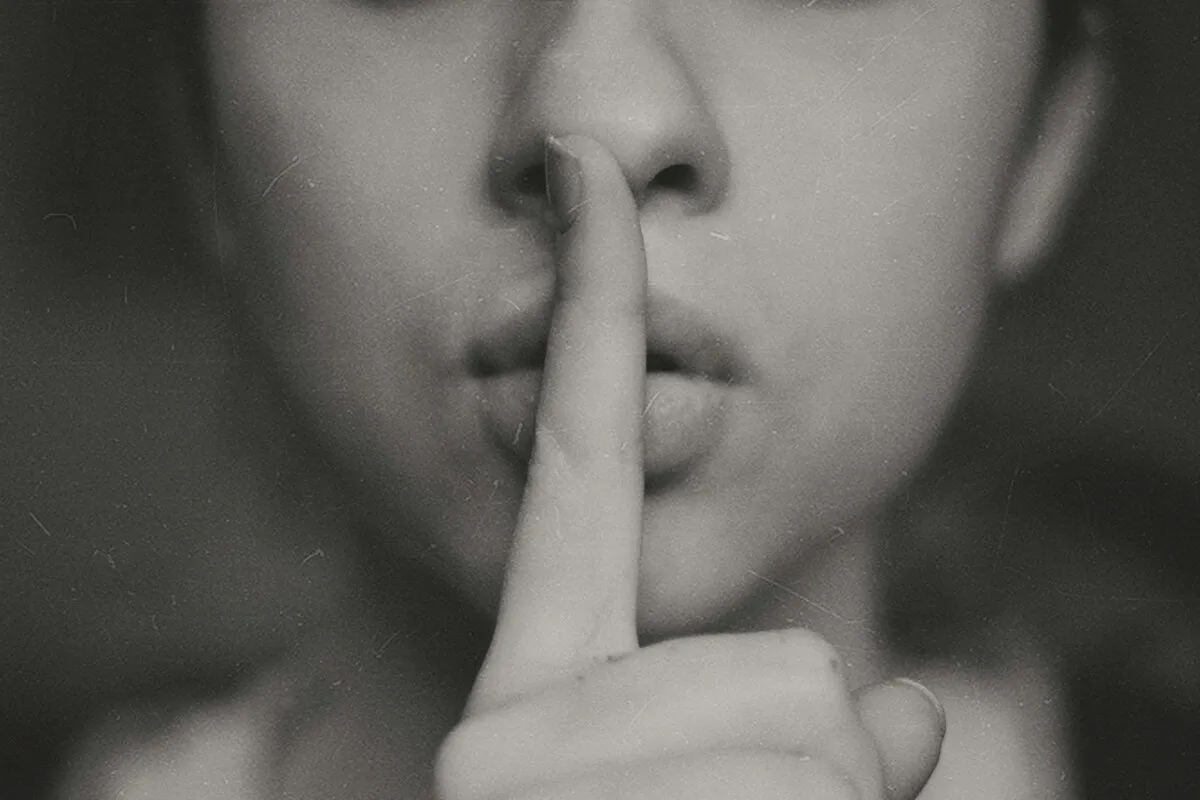 Pessoa fazendo gesto de silêncio com o dedo indicador sobre os lábios em imagem em preto e branco