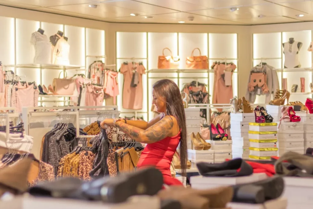 Mulher em uma loja de roupas e sapatos, olhando uma peça de roupa em um cabide, cercada por itens femininos, simbolizando a busca por renda extra através de vendas ou comércio.