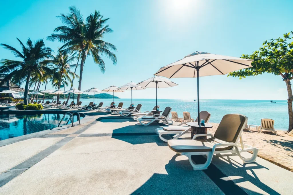 Resorts all inclusive: Espreguiçadeiras e guarda-sóis à beira da praia e da piscina em um resort tropical.