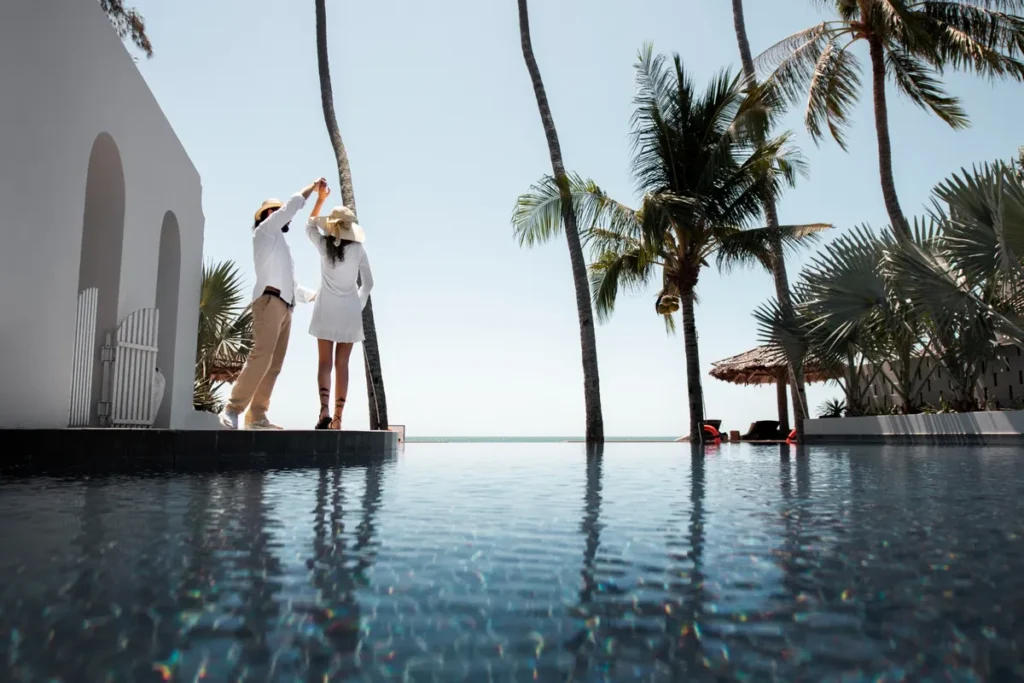Resorts all inclusive: Casal de férias dançando à beira de uma piscina com borda infinita em resort tropical.