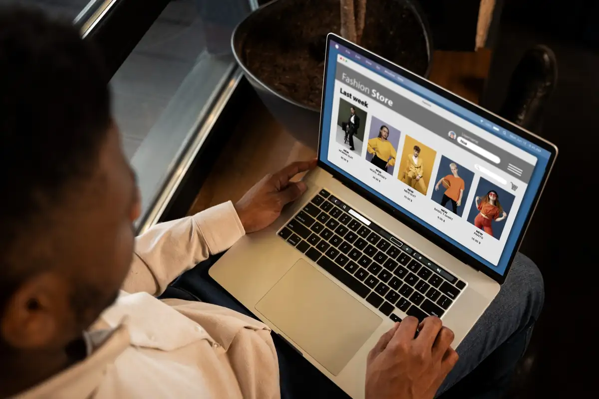 Pessoa navegando em loja virtual de roupas pelo notebook, avaliando opções de vestuário com foco em usabilidade e experiência do usuário.