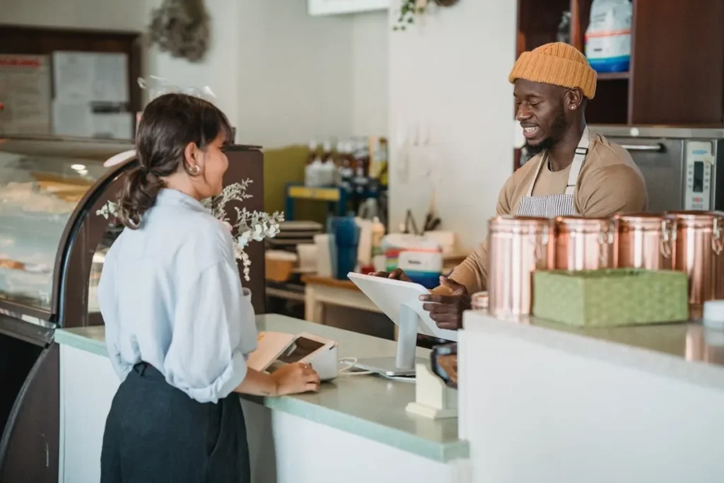 Atendente sorridente interagindo com cliente em balcão de café, demonstrando excelente CX e atendimento personalizado.