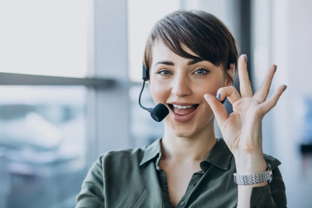 Mulher sorridente com headset fazendo sinal de OK, representando a eficiência e sucesso na resolução de problemas (FCR).
