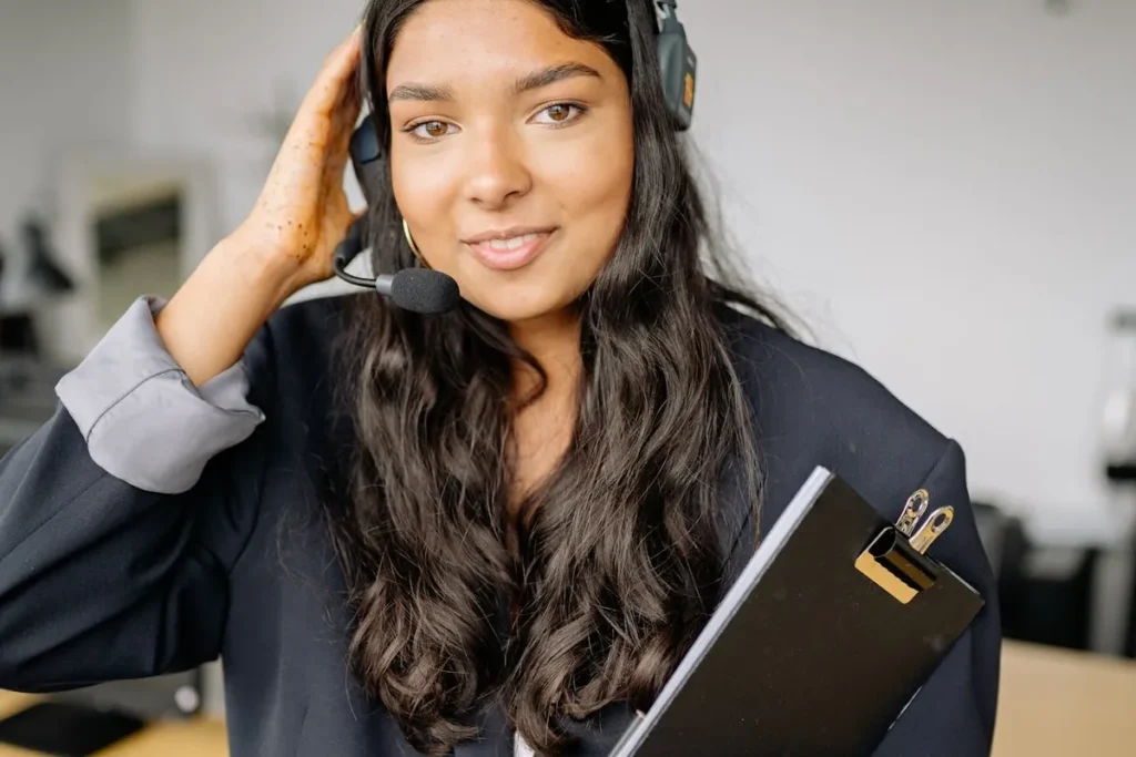 Mulher jovem e sorridente, com fone de ouvido de call center, segurando uma prancheta preta. Profissional de atendimento ao cliente.