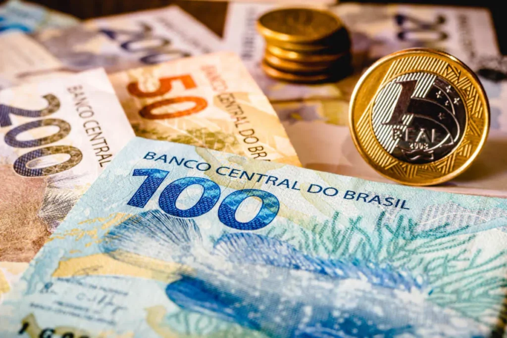 Moedas e notas de dinheiro brasileiro, como a moeda de 1 real e notas de 50, 100 e 200 reais, representando o conceito de renda extra.