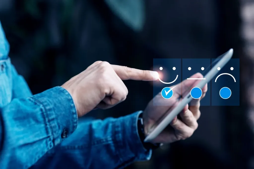 Uma mão tocando a tela de um tablet para selecionar o emoji de rosto sorridente em uma pesquisa de satisfação.