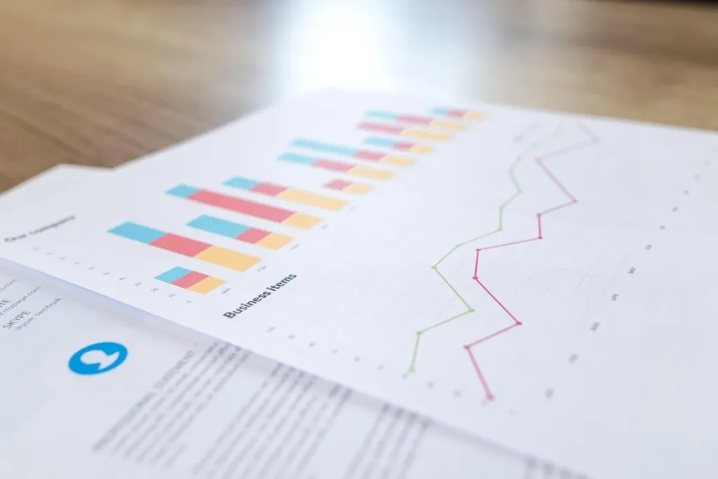 Documentos impressos com gráficos de barras coloridos e linhas de tendência em papel, representando a análise de dados e a comparação com benchmarks.