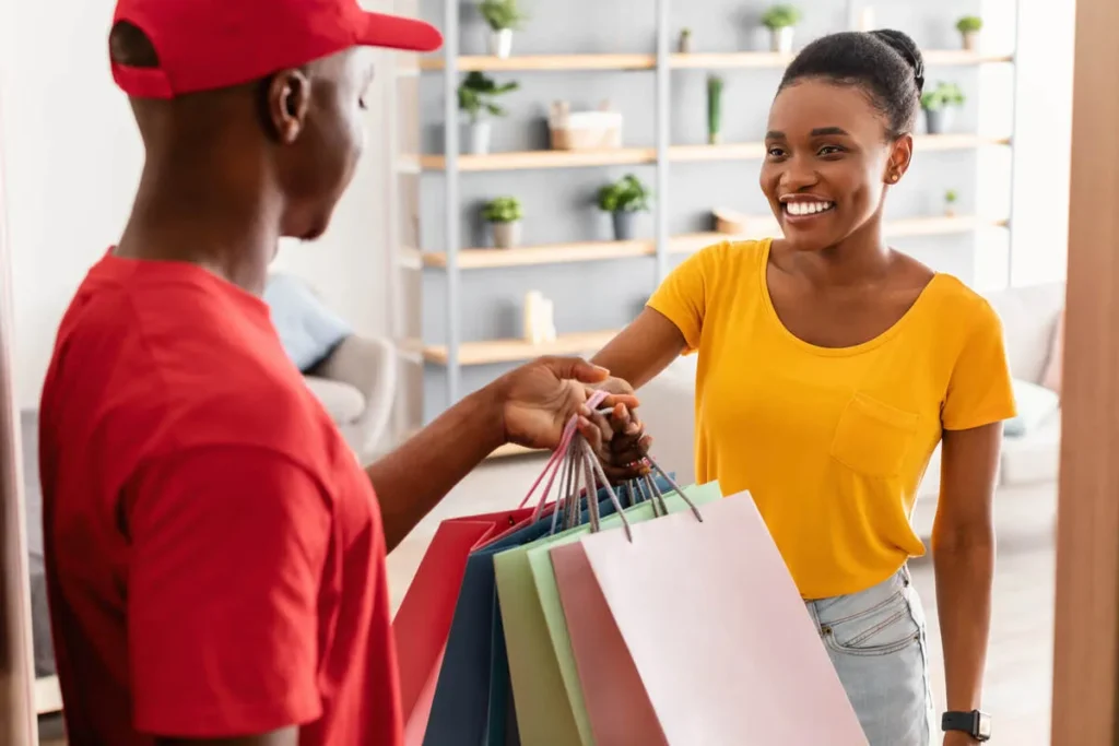 Uma mulher sorridente recebe sacolas de compras de um entregador, simbolizando o comércio varejista online.