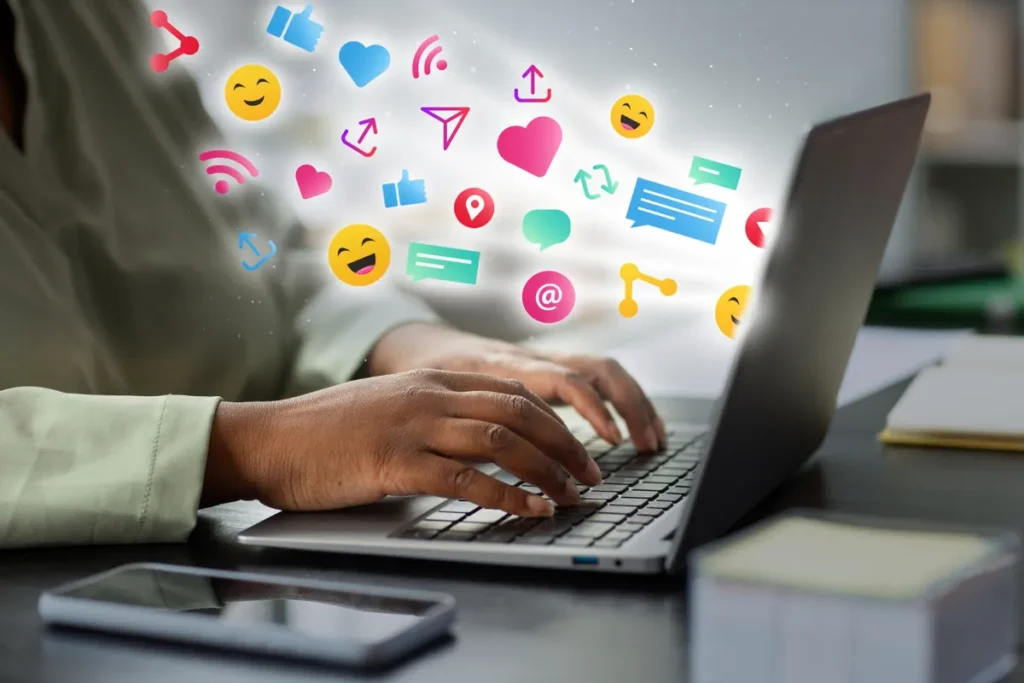 Mãos de uma pessoa digitando em um laptop, com ícones de redes sociais e de comunicação flutuando na tela, representando o endomarketing digital.