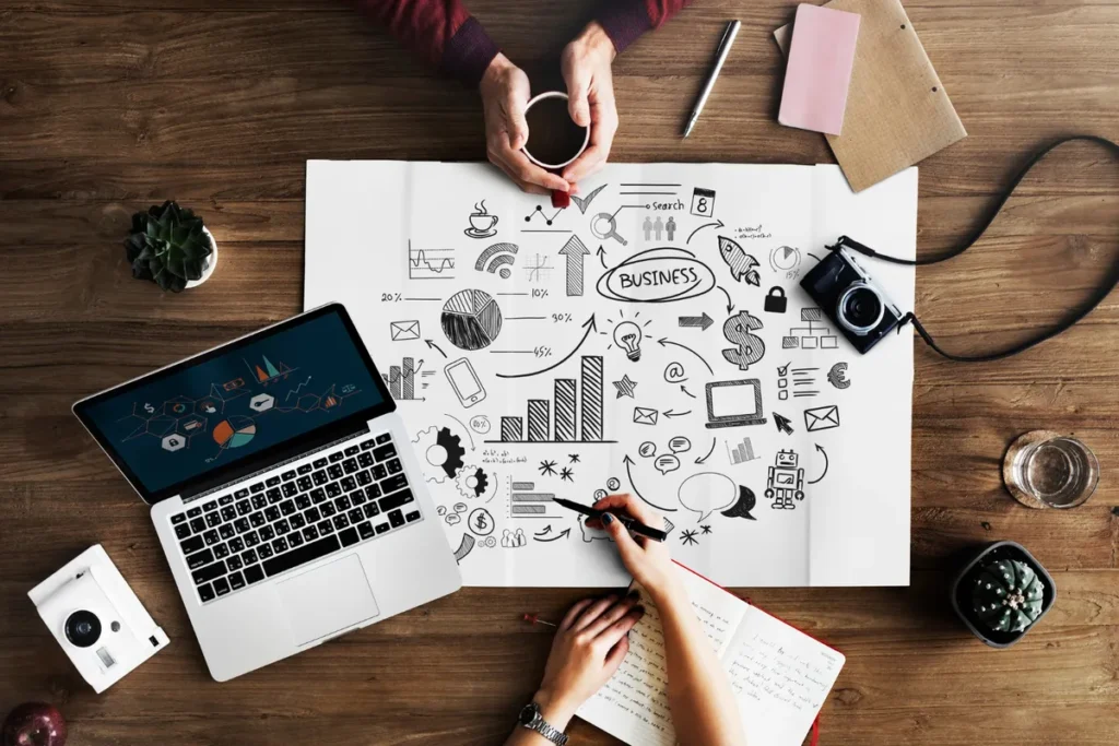 Visão superior de duas pessoas em uma mesa de madeira, desenvolvendo ideias de endomarketing em um grande papel com desenhos de brainstorming e gráficos.