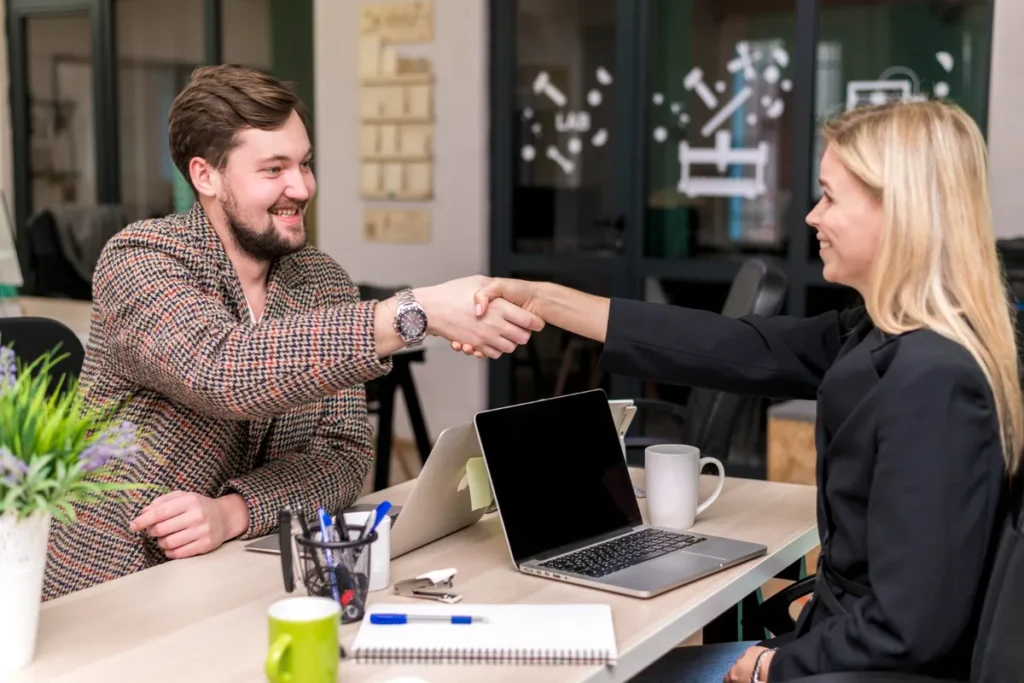 Dois profissionais sorridentes apertando as mãos após uma reunião de negócios, simbolizando um follow up bem-sucedido.