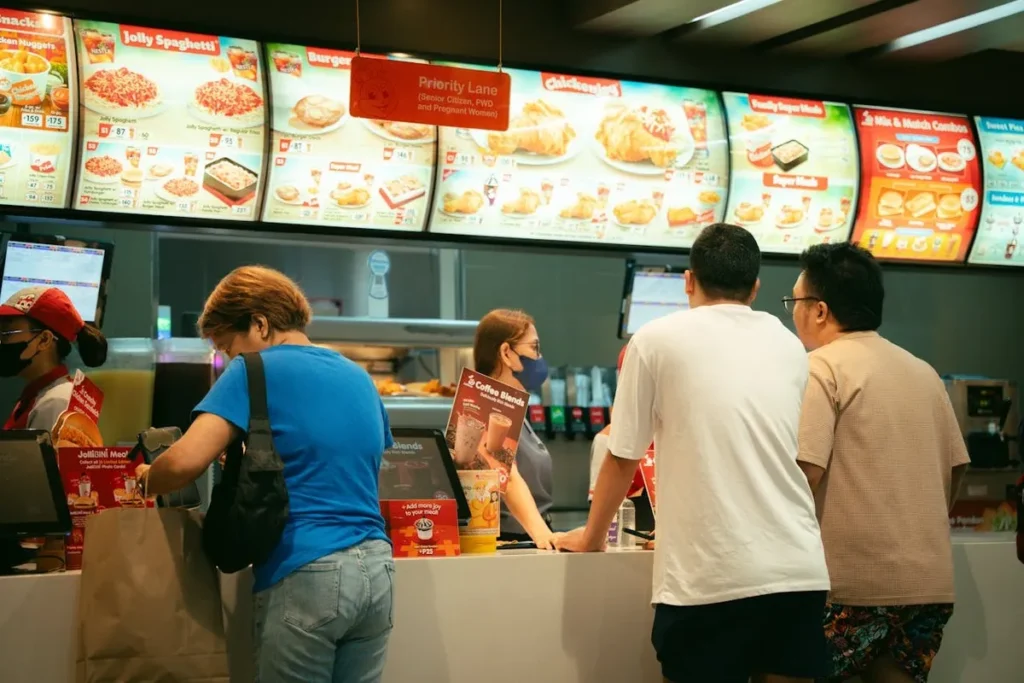 Pessoas em uma lanchonete, fazendo pedidos em um balcão com um grande menu ao fundo.