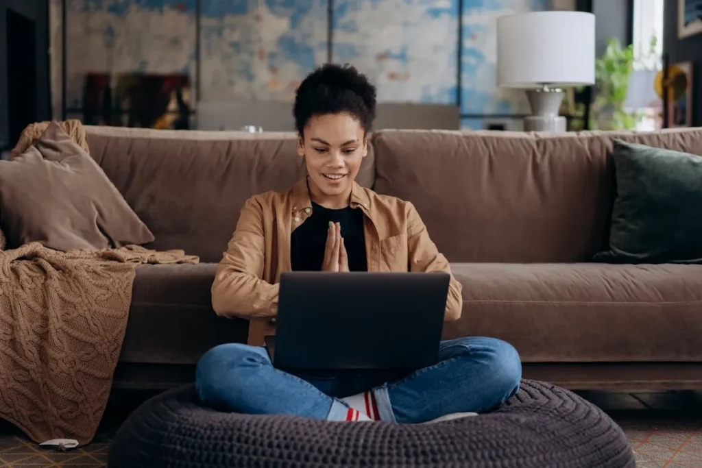 Mulher sorrindo, sentada no chão com um notebook, em posição de meditação, simbolizando tranquilidade ao ganhar dinheiro avaliando empresas online.