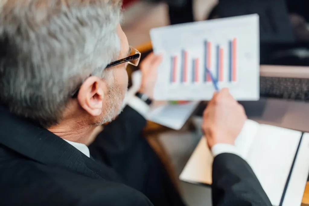 Executivo analisando gráfico de barras colorido durante reunião de negócios, simbolizando avaliação de desempenho e tomada de decisões estratégicas.