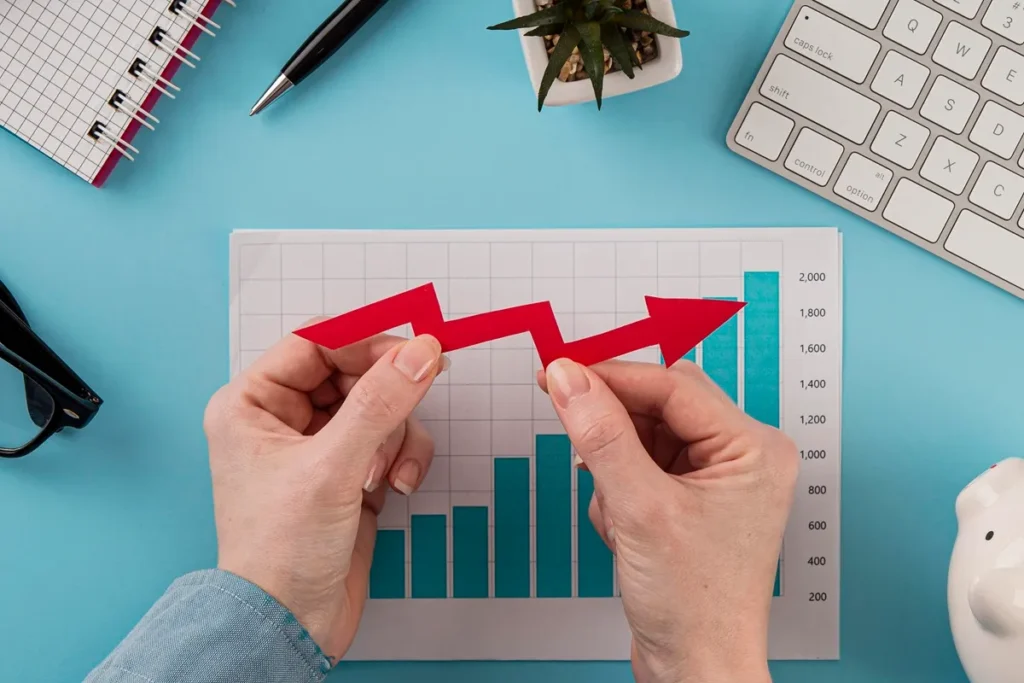 Mãos segurando seta vermelha apontando para cima sobre gráfico de barras, simbolizando crescimento financeiro e aumento de resultados.
