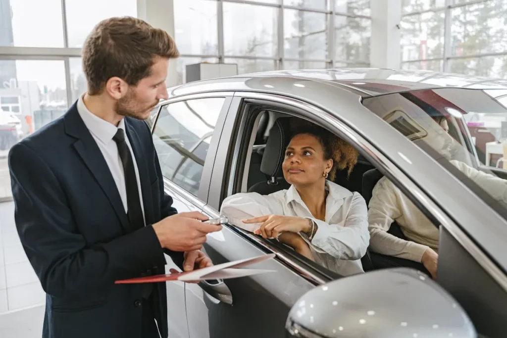 Vendedor de carros conversando com cliente em um showroom, oferecendo incentivo para a compra de um veículo.