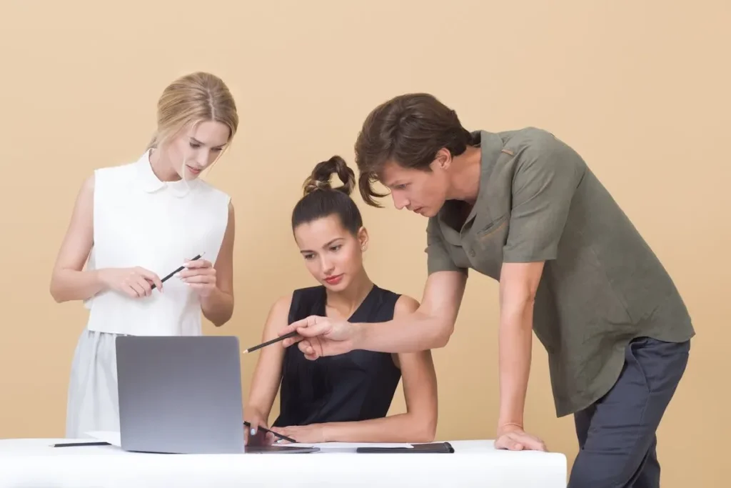 Equipe de profissionais colaborando ao redor de um laptop, com um colega oferecendo incentivo e orientação.