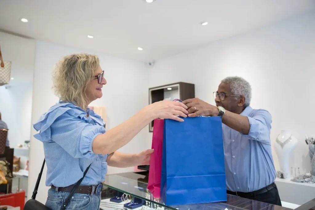 Mulher recebendo sacolas de compras de vendedor, demonstrando know how no atendimento ao cliente.