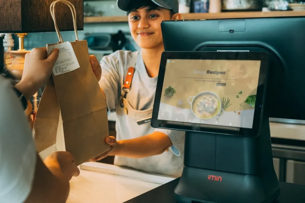 Funcionário entregando sacola de papel com know how em atendimento ao cliente e tecnologia de ponto de venda iMin.