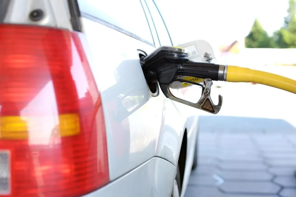 Bico de abastecimento amarelo e preto inserido no tanque de um carro branco em um posto de combustível, representando o serviço oferecido pelas redes de postos.