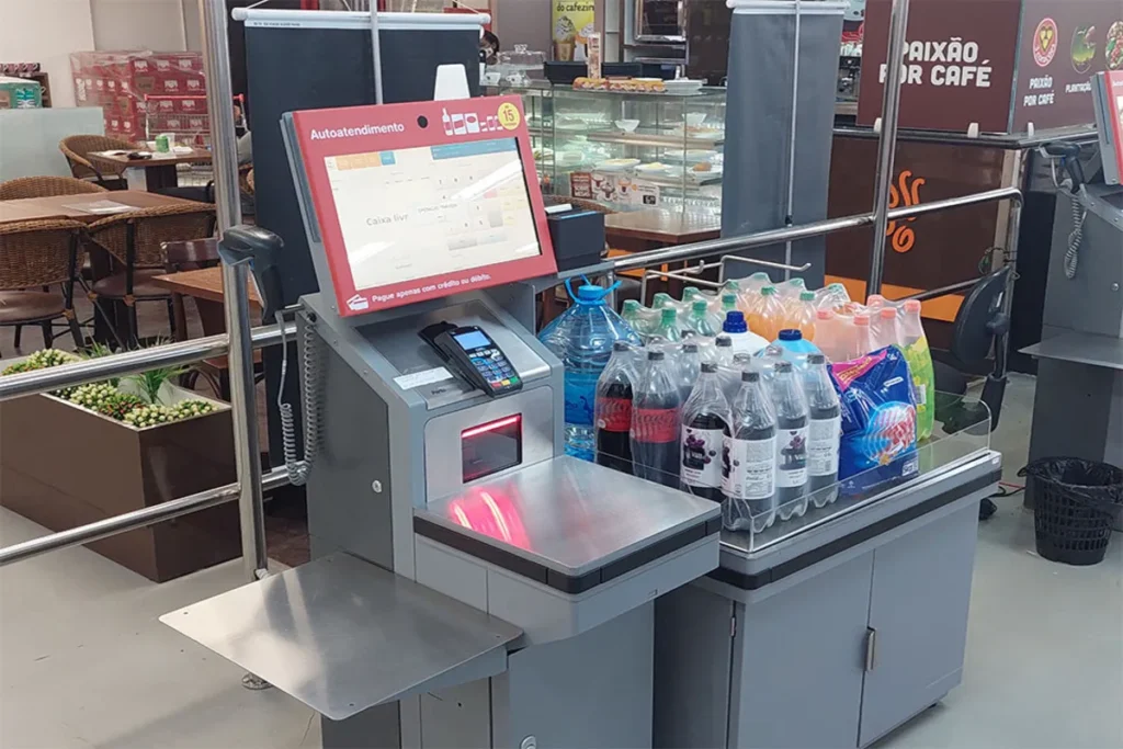 Terminal de self-checkout em um supermercado com produtos na balança, ilustrando a tecnologia de autoatendimento e o processo de pagamento autônomo.