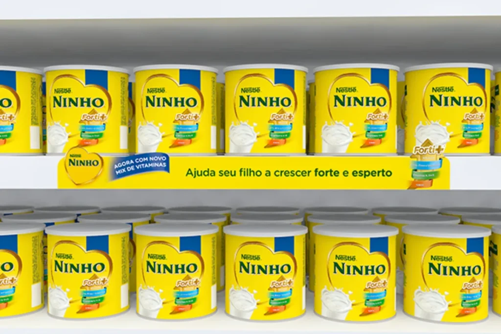 Uma prateleira de supermercado com latas de leite em pó da marca Ninho e um banner de MPDV (Material de Ponto de Venda) no centro. A imagem ilustra como as estratégias de MPDV são usadas para destacar um produto para o público-alvo, reforçando os benefícios do produto e impulsionando as vendas.