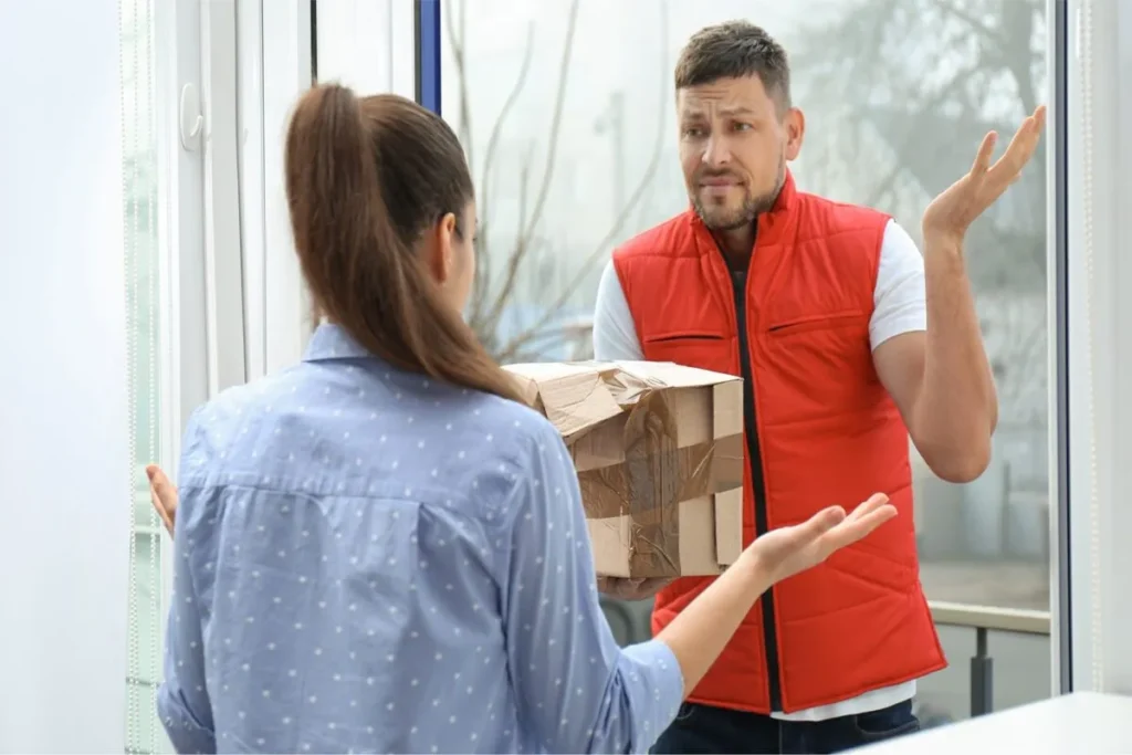 Cliente gesticulando para um entregador que segura uma caixa amassada na porta, ilustrando uma falha no serviço de entrega.