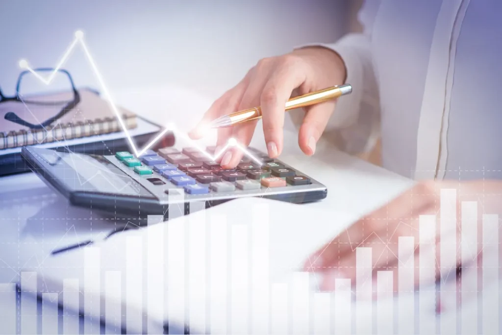 Pessoa de negócios usando uma calculadora para analisar o faturamento, com gráficos de crescimento e finanças sobrepostos digitalmente na imagem.