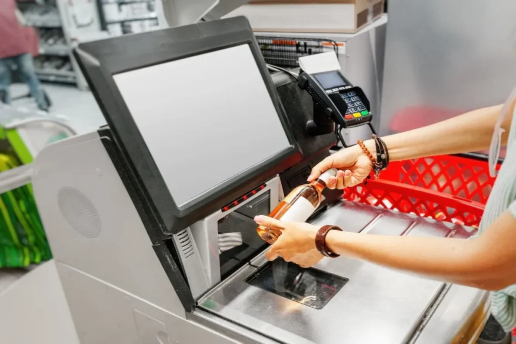 Cliente usando um self-checkout para escanear uma garrafa, mostrando a praticidade do autoatendimento em supermercados e lojas de varejo.