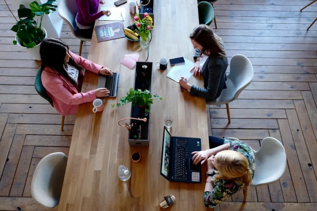Equipe feminina fazendo planejamento estratégico em uma longa mesa de escritório, com laptops e anotações.
