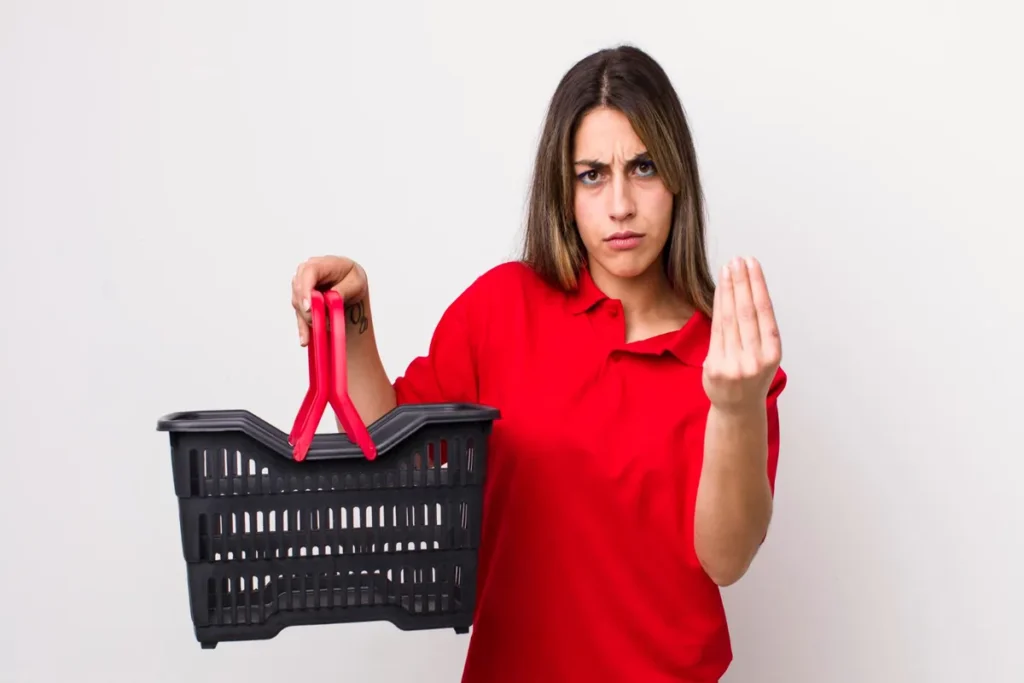 Uma mulher com expressão de insatisfação segurando uma cesta de compras vazia e fazendo um gesto de questionamento com a mão.