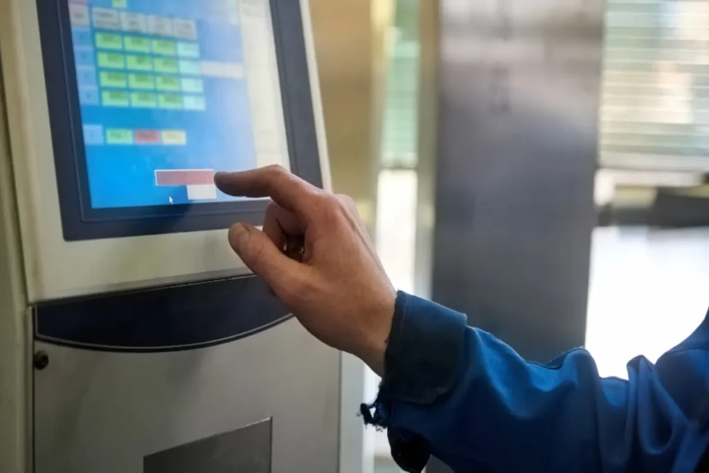 Uma mão de operário tocando um tóten de atendimento com uma tela de pedidos.