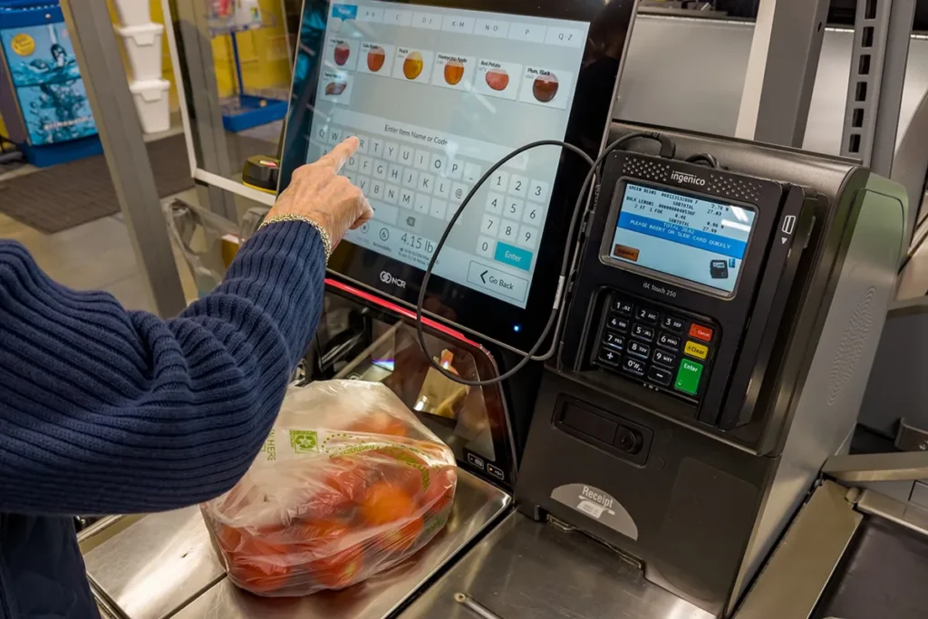 Uma pessoa usando um tóten de atendimento em um supermercado para pesar produtos e digitar informações na tela.
