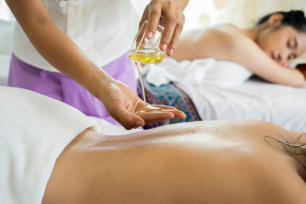 Uma massagista em um spa, derramando óleo de massagem na mão antes de aplicar nas costas de uma cliente. A imagem retrata um tratamento de massagem, com o foco em relaxamento e bem-estar em um dos muitos SPAs que oferecem serviços de beleza e saúde.