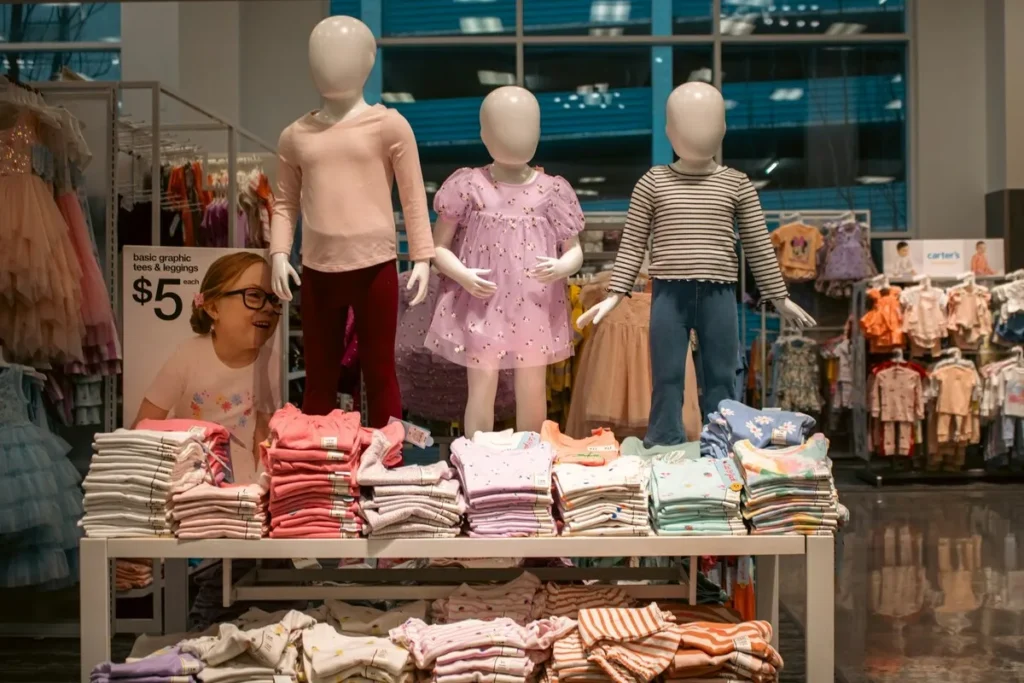 Manequins infantis em uma mesa de exposição, exibindo roupas casuais. A imagem mostra pilhas de roupas infantis dobradas e o ambiente de uma das muitas lojas infantis em que se pode encontrar roupas para crianças.