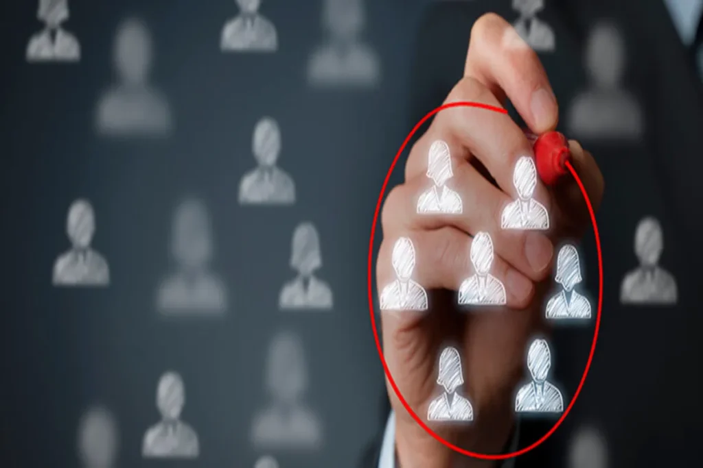 Mão desenhando um círculo vermelho em uma tela de toque, selecionando um grupo de ícones de pessoas (avatares) de um conjunto maior. A imagem simboliza a amostragem estatística e a segmentação de mercado.